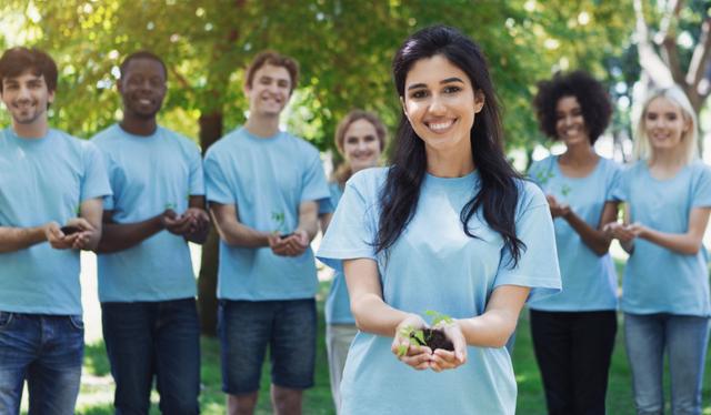 ”Young volunteers in blue t-shirts enjoying planting trees together.”